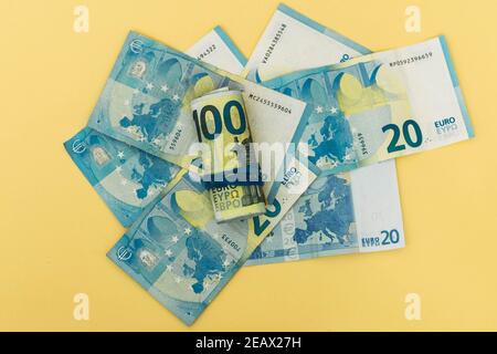 Selektiver Fokus auf mehrere zwanzig Euro-Banknoten und andere Banknoten Aufgerollt und von einem Gummiband auf einem gehalten Gelber Hintergrund Konzept sparendes Sparen Stockfoto