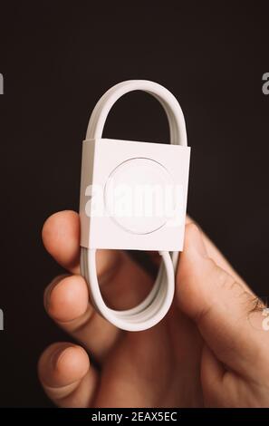 Paris, Frankreich - 4. Oktober 2018: POV close-up männliche Hand hält vor schwarzem Hintergrund neues Paket des ausgepackten Apple Watch Magnetic Charger auf USB-C Kabel Stockfoto