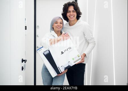 Frau überrascht ihren Bruder mit einer Sony playstation 5-Konsole der nächsten Generation, Online-Shopping-Geschenk, moderne Videospiel-Gerät für Cyber-Sport. Moskau - Stockfoto