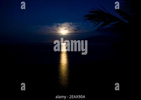 Vollmonduntersetzung durch Wolken und Reflektion auf der Oberfläche des Meeres im tropischen Hawaii. Stockfoto