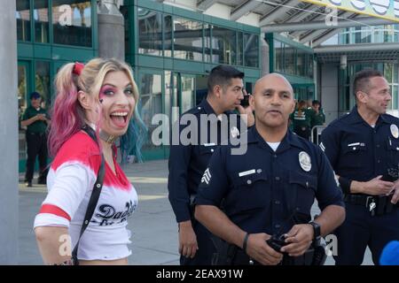 Ein Cosplayer, der als Harley Quinn aus dem DC-Universum gekleidet ist, posiert neben drei diensthabenden LAPD-Polizisten lächelnd. Stockfoto