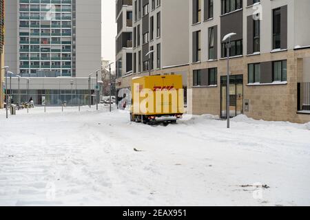 DHL-Lieferservice mit einem gelben LKW in einem Wohngebiet. Viel Schnee behindert die Arbeit. Stockfoto