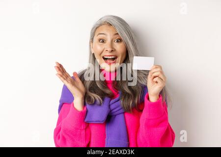 Einkaufskonzept. Glücklich asiatische alte aldy suchen beeindruckt und zeigt Kunststoff-Kreditkarte ihrer Bank, über weißem Hintergrund stehen Stockfoto