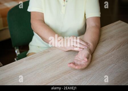 Reife Frau, die ihren Puls nimmt, während sie am Tisch sitzt Stockfoto