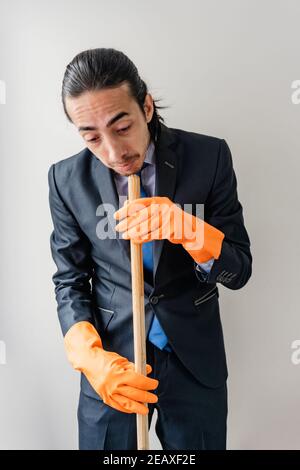 Geschäftsmann in blauen Anzug hält Haushaltsreinigungsbedarf, sehr verwirrt, Arbeitstag, Home Office Stockfoto