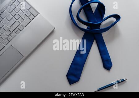 Foto von einem Arbeitsplatz zu Hause mit blauer Krawatte, einem modernen, ganz grauen Computer und einem Bleistift, Labor Day. Stockfoto