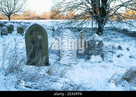 Grabsteine in St. Peter und St. Paul Kirchhof im Schnee. Long Compton, Warwickshire, England Stockfoto