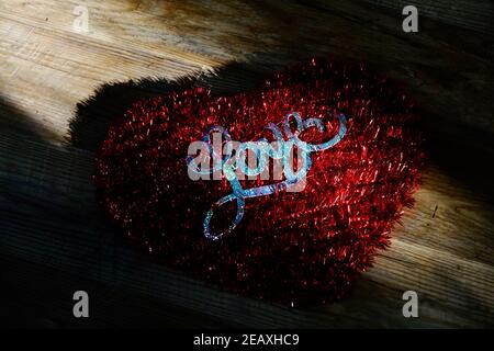 Ein rotes Herz mit dem Wort Liebe, das darauf geschrieben ist und von einem kleinen Lichtschacht ausgesetzt ist. Stockfoto