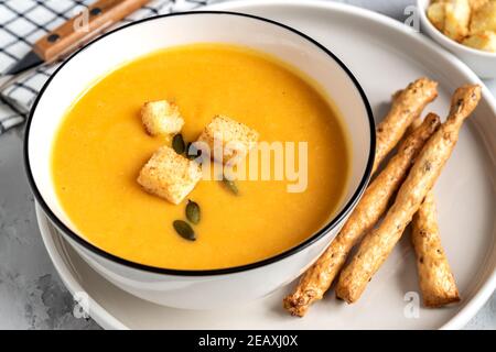 Nahaufnahme von Kürbis, Karottencremesuppe in einer Schüssel. Mit Croutons, Kürbiskernen und Brotsticks Stockfoto