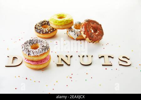 Mehrfarbige Donuts mit Glasur, Streuseln und der Inschrift Donuts auf weißem Hintergrund. Stockfoto