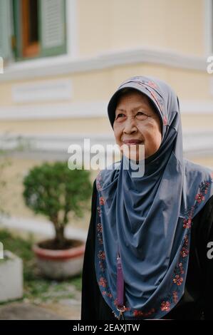 Ein älterer thailändischer muslimischer Frauenheld, der ein blaues Hijab-Kleid trägt und lächelt. Stockfoto