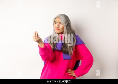 Mürrische asiatische Großmutter beschwert, zeigt italienisch, was Sie wollen Geste, schüttelt die Finger und starrte wütend links auf den Kopierraum, über stehen Stockfoto