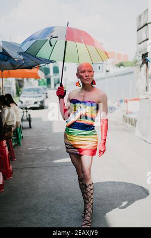 Porträt einer asiatischen queeren Person in Regenbogenfarben Kleid gekleidet, trägt rote Handschuhe und hält einen Regenbogenfarben Regenschirm in Bangkok Thailand. Stockfoto