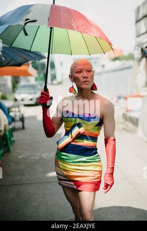 Porträt einer asiatischen queeren Person in Regenbogenfarben Kleid gekleidet, trägt rote Handschuhe und hält einen Regenbogenfarben Regenschirm in Bangkok Thailand. Stockfoto