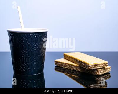 Schwarzer Einwegbecher aus Papier für Kaffeegetränke und Waffelplätzchen auf dem Tisch. Kaffee Getränk Waffel Dessert. Street Cafe. Papierbecher. Einwegtischwar Stockfoto