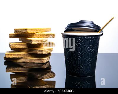 Schwarzer Einwegbecher aus Papier für Kaffeegetränke und Waffelplätzchen auf dem Tisch. Kaffee Getränk Waffel Dessert. Street Cafe. Papierbecher. Einwegtischwar Stockfoto