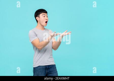 Asian Mann Heben Hände mit schockiert Gesicht Blick auf leer Raum beiseite isoliert auf Studio hellblauen Hintergrund Stockfoto