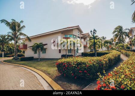 Schöner Hinterhof mit Garten vor einem zweistöckigen Haus. Tropisches Luxushaus mit Palmen und grünem Gras. Cottage umgeben von Palmen Stockfoto