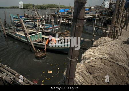 Ein Arbeiter, der Rattan-Körbe auf Meerwasser von einem Boot waschen, das an den Landungsstrand von Kamal Muara gebunden ist, einem Fischerdorf, das auch als grünes Muschelproduktionszentrum im Küstengebiet von Jakarta, Indonesien, bekannt ist. Stockfoto