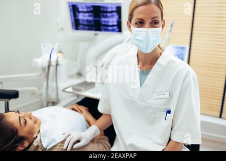 Frau Zahnarzt trägt Gesichtsmaske wegschauen, während eine Behandlung bei weiblichen Patienten in ihrer Klinik. Stockfoto