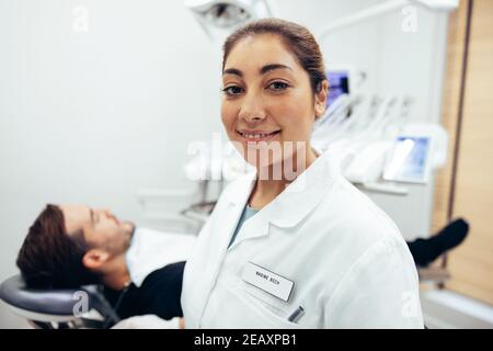 Porträt eines selbstbewussten Zahnarztes mit Patient im Zahnarztstuhl auf dem Rücken. Weibliche Zahnärztin in ihrer Klinik. Stockfoto