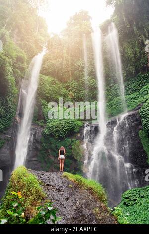 Gebräuntes Mädchen, das auf einem Stein vor einem Wasserfall steht.leichte Tonung. Stockfoto