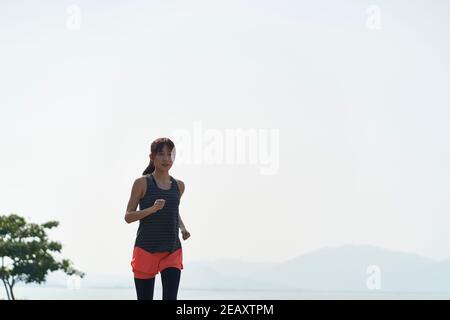 Junge asiatische Frau Jogger läuft in Seaside Park Stockfoto