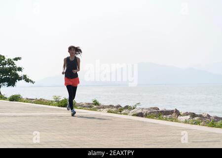 Junge asiatische Frau Jogger läuft in Seaside Park Stockfoto