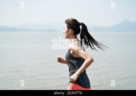 Junge asiatische Frau weibliche Läuferin läuft am Meer Stockfoto