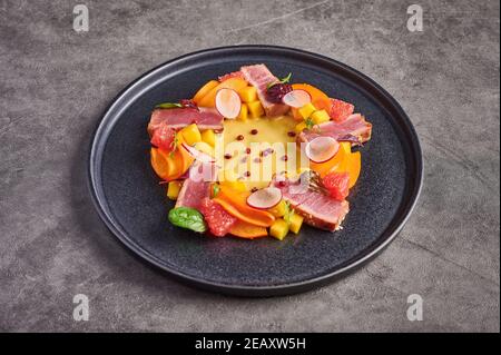 Hausgemachter Salat mit Thunfischsteak, Mango-Sauce, Kräutern und Gewürzen auf dunklem Teller, Nahaufnahme, Food Decorating Konzept Stockfoto
