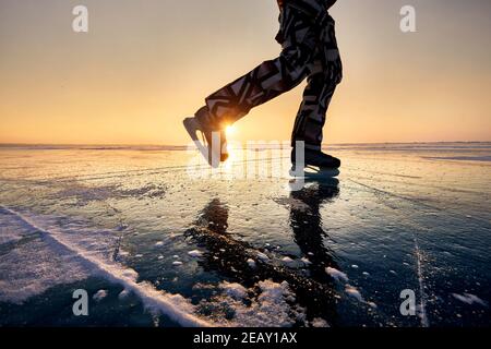 Nahaufnahme der Beine des Mannes mit Eislaufen in Silhouette Am gefrorenen See gegen schönen orangefarbenen Sonnenaufgang Stockfoto