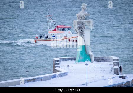 Sassnitz, Deutschland. Februar 2021, 11th. Das Rettungsboot der Seeretter passiert den eisigen Leuchtturm am Wellenbrecher des Hafeneingangs. Eisige Witterung und Schneefall behindern den Verkehr in Norddeutschland. Quelle: Jens Büttner/dpa-Zentralbild/dpa/Alamy Live News Stockfoto