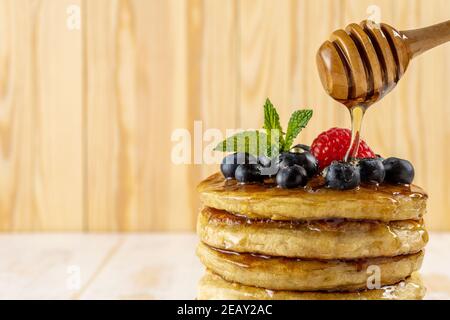 Leckere Pfannkuchen mit frischen Beeren und tropfendem Honig auf Holzhintergrund. Food-Konzept. Stockfoto