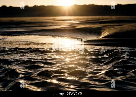 Kleine Wellen am Strand durch die Änderung der Gezeiten in der Morgensonne. Stockfoto