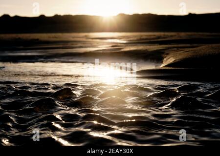 Kleine Wellen am Strand durch die Änderung der Gezeiten in der Morgensonne. Stockfoto