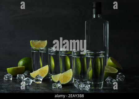 Flasche Wodka, Schüsse, Eiswürfel und Limettenscheiben auf schwarzem Rauchtisch Stockfoto