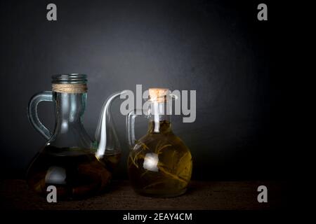 Natives Olivenöl extra. Zwei Ölkrug mit extra nativem Olivenöl gewürzt mit Ruderer und Knoblauch auf einem dunklen Hintergrund. Stockfoto