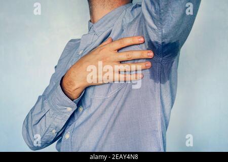 Mann mit Hyperhidrose Schwitzen sehr schlecht unter Achselhöhle in blauem Hemd. Nasser Fleck auf meinem Hemd vor Schweiß. Stockfoto