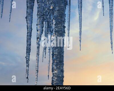 Eiszapfen an einem frostigen Wintertag. Die Sonne geht unter mit blauen und orangen Farben im Hintergrund. Stockfoto