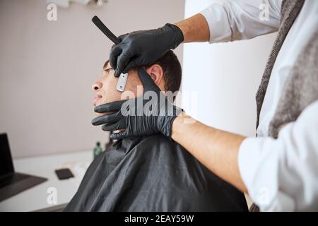 Fokussiertes Bild von Mann Hand in Handschuhen halten Rasierklinge Und auf den Bart achten Stockfoto