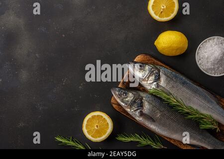 Zwei frische Seebassfische mit Rosmarin und Zitrone auf schwarzem Tisch. Meeresfrüchtekonzept. Stockfoto