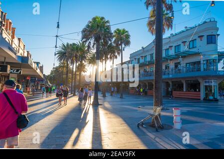 Menschen, die in Richtung der untergehenden Sommersonne entlang des Corso in der Küstenvorstadt von Sydney Manly, New South Wales, Australien, wandern Stockfoto