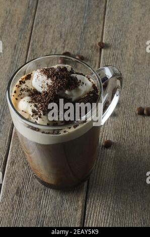 Glas Tasse Kaffee mit Milch, Eis und geriebener Schokolade auf einer Holzoberfläche mit gerösteten Kaffeebohnen. Selektiver Fokus. Stockfoto