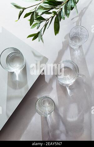 Gläser Wasser Draufsicht Sommer Komposition auf hellem Hintergrund. Stillleben mit Olivenzweig und langen Schatten, mit Kopierraum Stockfoto