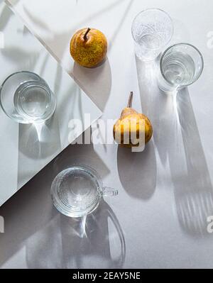 Minimalistisches Stillleben von Birnen und Wassergläsern von oben. Sommer Komposition Licht und Schatten auf einem grauen Tisch Stockfoto