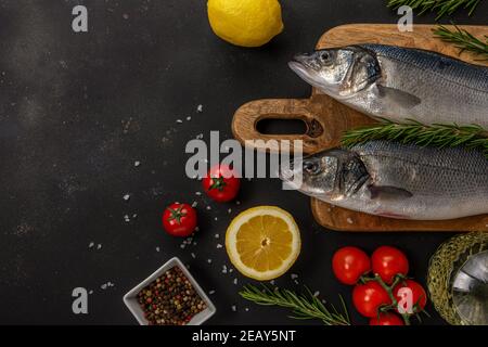 Zwei frische Seebaßfische mit Rosmarin und Gemüse auf schwarzem Tisch. Meeresfrüchtekonzept. Stockfoto