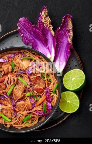 Pancit Bihon in schwarzer Schale auf dunkler Schieferplatte. Filipino Küche Nudeln Gericht mit Schweinebauch, Huhn, Gemüse. Asiatische Küche. Draufsicht Stockfoto