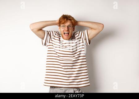 Frustrierter Rotschopf Mann in Panik, schreiend und Hände am Kopf haltend, auf weißem Hintergrund stehend Stockfoto