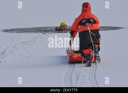 11. Februar 2021, Brandenburg, Potsdam: Andy Hertel (l.), Feuerwehrchef der Berufsfeuerwehr Potsdam, stürzte bei einer Übung in das dünne Eis des Tiefensees ein. Am selben Tag hatte die Potsdamer Berufsfeuerwehr das aktuelle winterliche und kalte Wetter genutzt, um die Rettung von Menschen aus dem Eis und das Tauchen unter realen Bedingungen zu üben. Rund 20 Mitglieder der Berufsfeuerwehr und der Polizeiwache Babelsberg waren an dieser Übung im tiefen See, am Steg der Schiffbauergasse, beteiligt. Foto: Patrick Pleul/dpa-Zentralbild/ZB Stockfoto