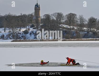 11. Februar 2021, Brandenburg, Potsdam: Charlotte Conrad (r), Feuerwehrchefin, und Andy Hertel, Feuerwehrchefin der Potsdamer Berufsfeuerwehr, trainieren die Rettung einer im Eis eingestürzten Person. Im Hintergrund ist der Flatow Tower im Park Babelsberg zu sehen. Am selben Tag nutzte die Potsdamer Berufsfeuerwehr das aktuelle winterliche und kalte Wetter, um die Rettung von Menschen aus Eis und Eistauchen unter realen Bedingungen zu üben. Etwa 20 Mitglieder der Berufsfeuerwehr und der Polizeiwache Babelsberg waren an dieser Übung im tiefen See, AT, beteiligt Stockfoto